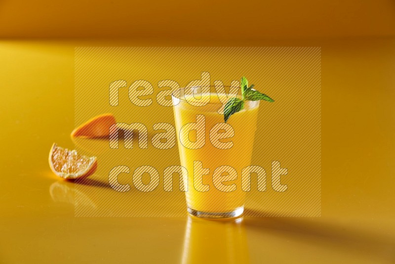 glass of orange juice with  mint on yellow background
