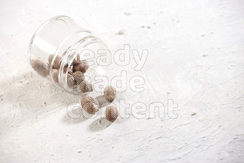 A glass jar full of nutmeg flipped and the seeds came out on a textured white flooring in different angles