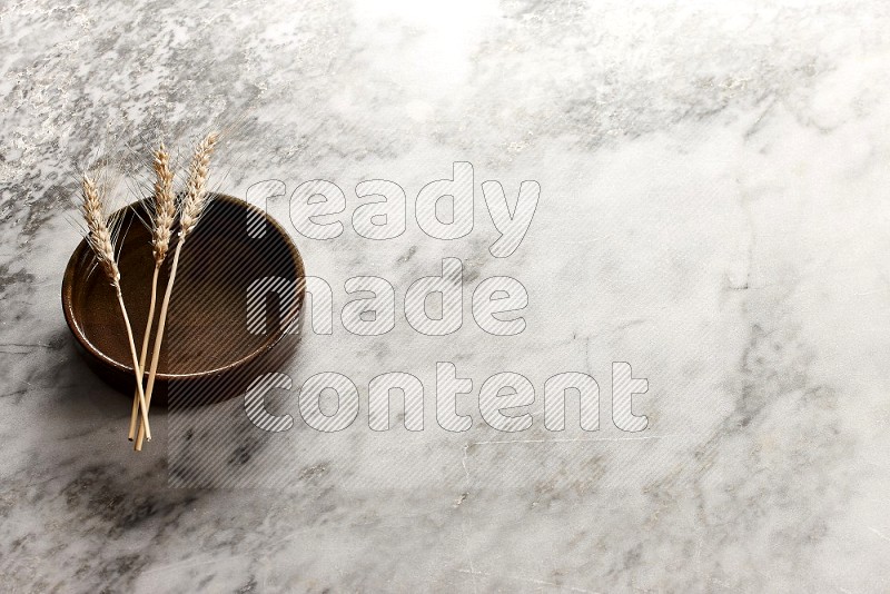 Wheat stalks on Multicolored Pottery Oven Plate on grey marble flooring, 45 degree angle