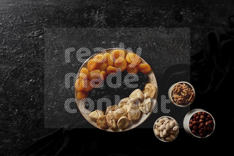 Dried fruits in a pottery bowl with nuts in a dark setup