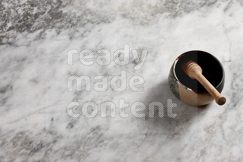 Multicolored Pottery bowl with wooden honey handle in it, on grey marble flooring, 65 degree angle