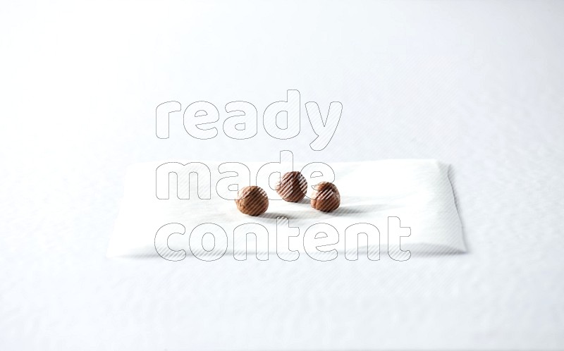 3 peeled hazelnuts on a piece of paper on a white background in different angles