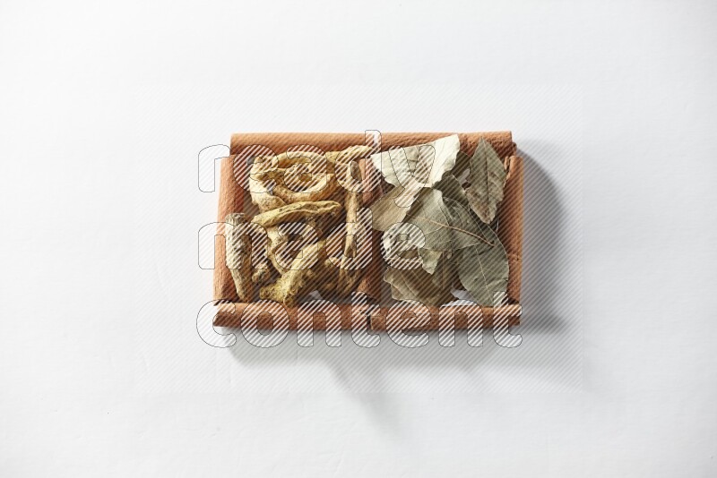 مربعان من أعواد القرفة ممتلئان بأصابع الكركم وأوراق الغار علي خلفية بيضاء