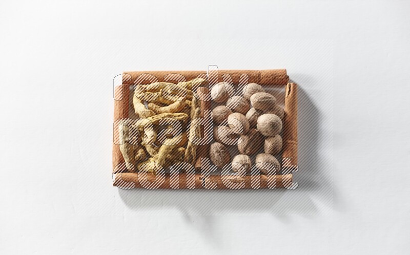 مربعان من أعواد القرفة ممتلئان بأصابع الكركم  وجوزة الطيب علي خلفية بيضاء