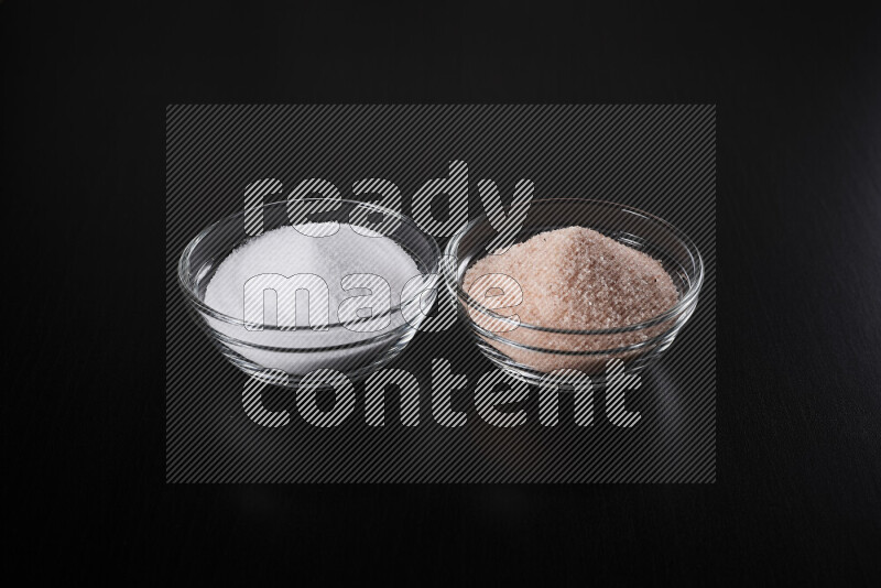 2 glass bowls one is filled with himalayan salt and the other with white salt on black background