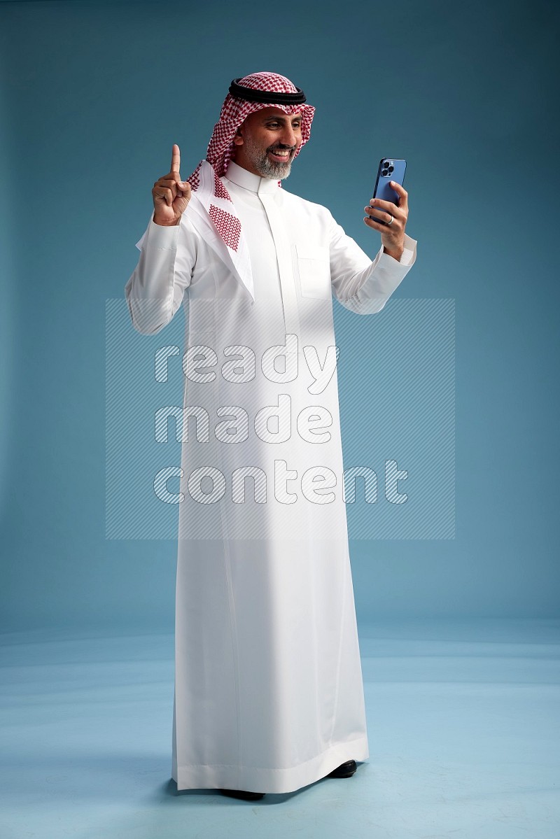 Saudi man wearing thob and shomagh texting on blue background