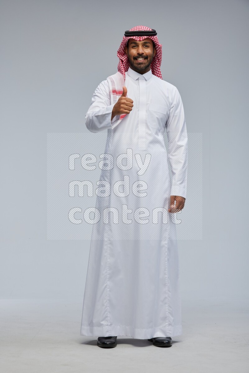 Saudi man Wearing Thob and shomag standing interacting with the camera on Gray background