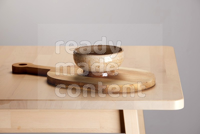 multi colored bowl placed on a  wooden oval cutting board on the edge of wooden table