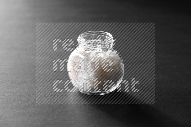 A glass spice jar full of salt on black flooring