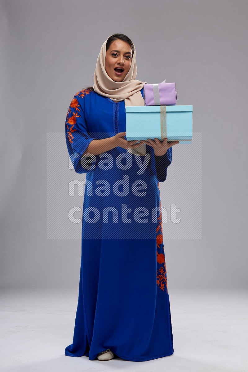 A Saudi woman standing wearing Jalabeya holding a gift box