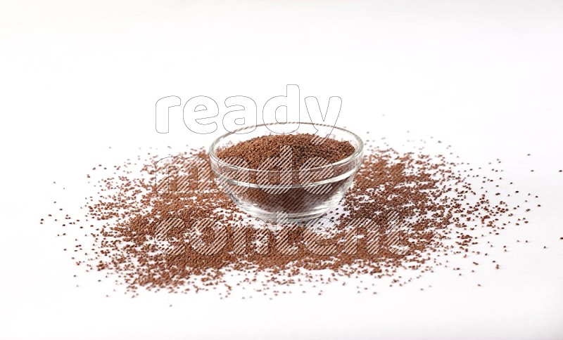 A glass bowl full of garden cress seeds with more seeds spread on a white flooring