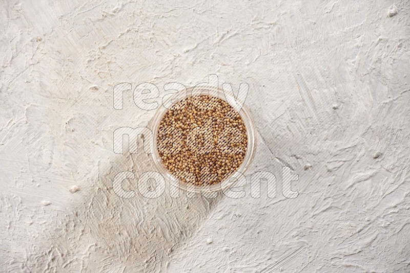 A glass jar full of mustard seeds on a textured white flooring in different angles