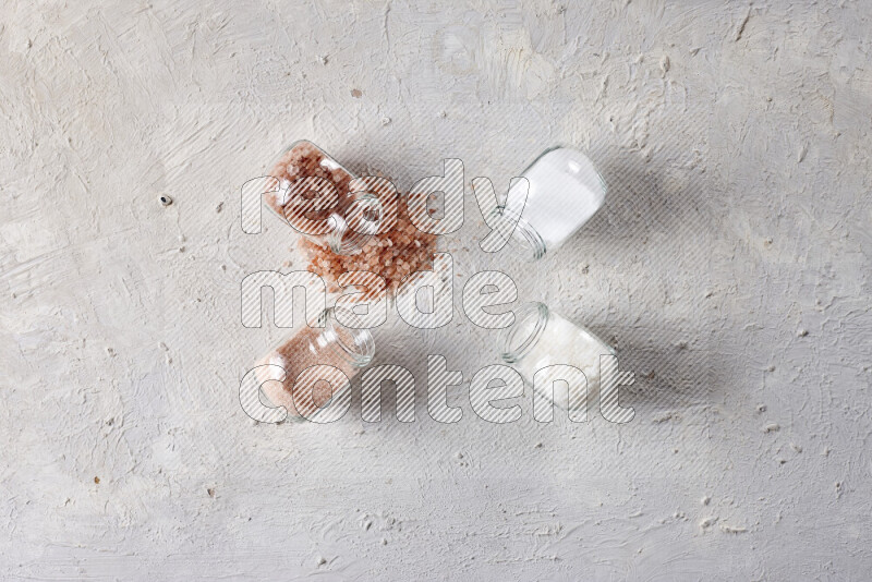 4 glass jars filled with table salt, coarse sea salt, fine himalayan salt and coarse himalayan salt on white background