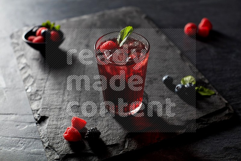 A glass of mixed berries juice with mint leaves on black background