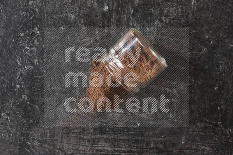 A flipped glass jar full of cloves powder on a textured black flooring