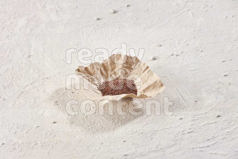 A crumpled piece of paper full of garden cress seeds on a textured white flooring