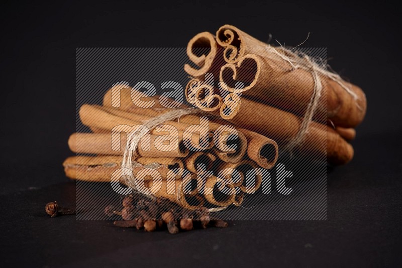 Two bounded stacks of cinnamon sticks with cloves on black background