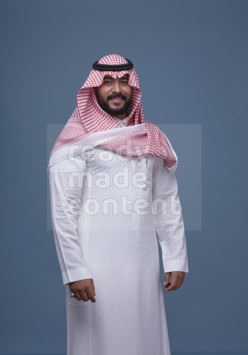 A Saudi man posing on blue background wearing Thob and Shomag