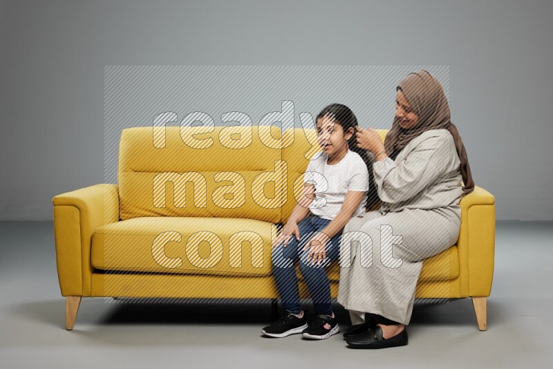 A mother sitting styling hair for her daughter on gray background