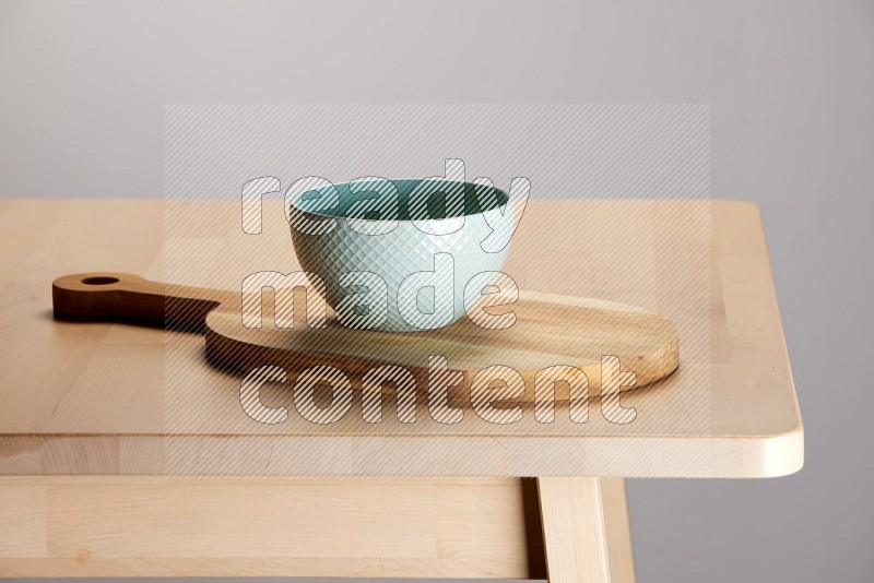 green bowl placed on a  wooden oval cutting board on the edge of wooden table