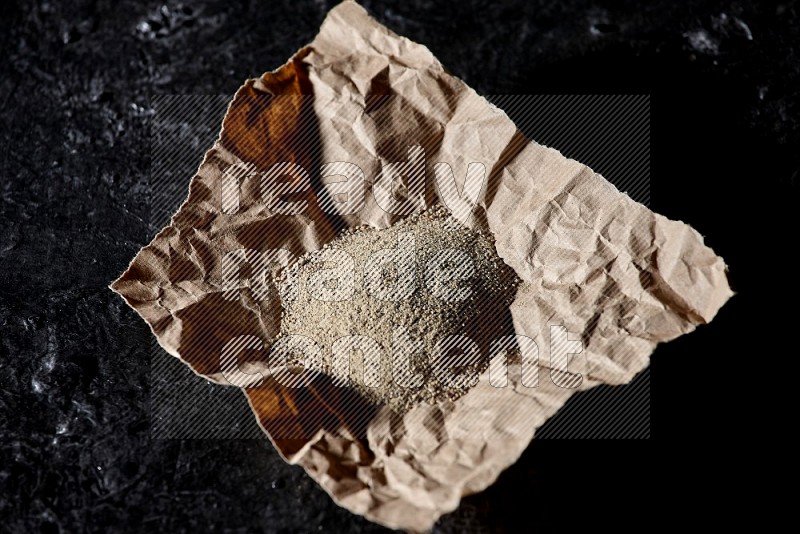 White pepper powder in a crumpled paper on textured black flooring