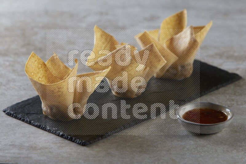 wonton cups with soy sauce ramkin on rectangle slate on grey textured counter top