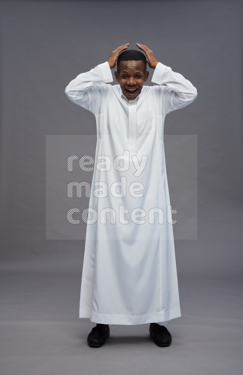 Saudi man wearing thob standing hands behind head on gray background