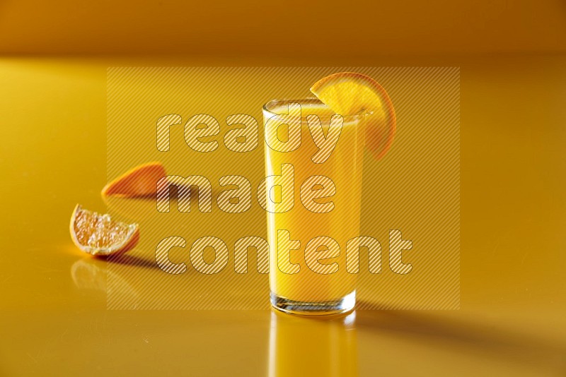 glass of orange juice with orange slice on yellow background
