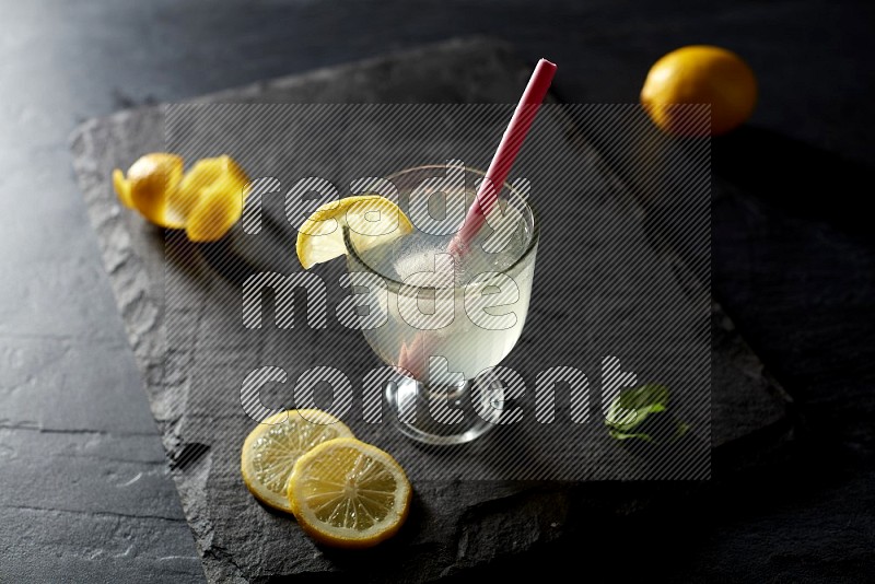 A glass of lemon juice with a straw on black background