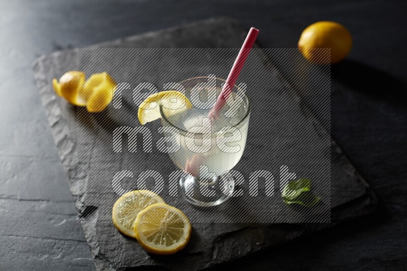 A glass of lemon juice with a straw on black background