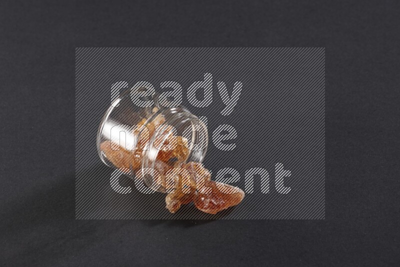 A glass jar full of gum arabic and jar is flipped and gum spread out on black flooring