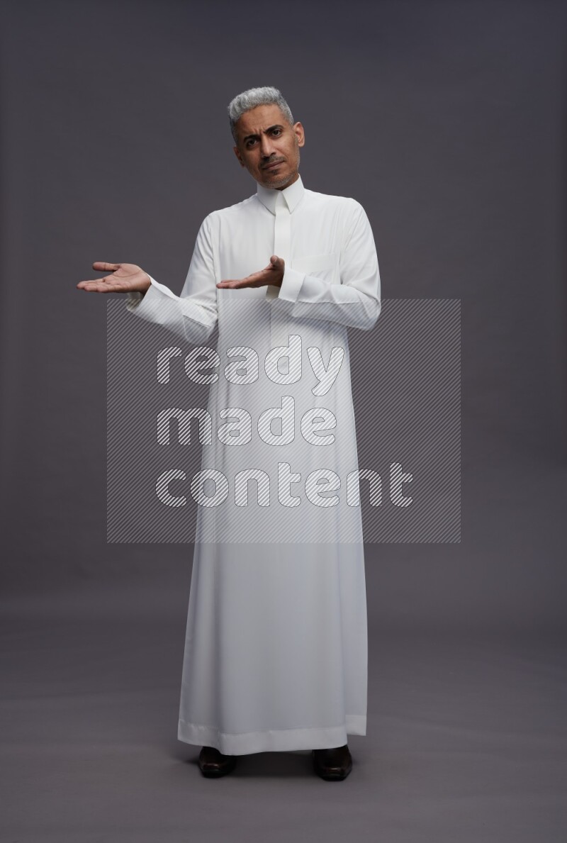 Saudi man wearing thob standing interacting with the camera on gray background