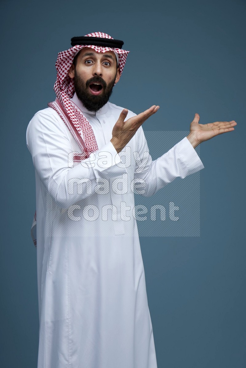 A man pointing in a blue background wearing Saudi Thob and Shomag