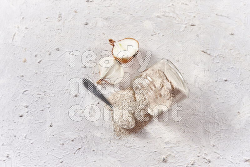 A glass jar full of onion powder flipped with some spilling powder on white background