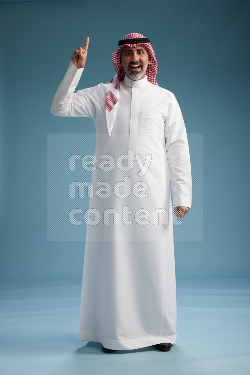 Saudi man wearing thob and shomagh posing to the camera on blue background