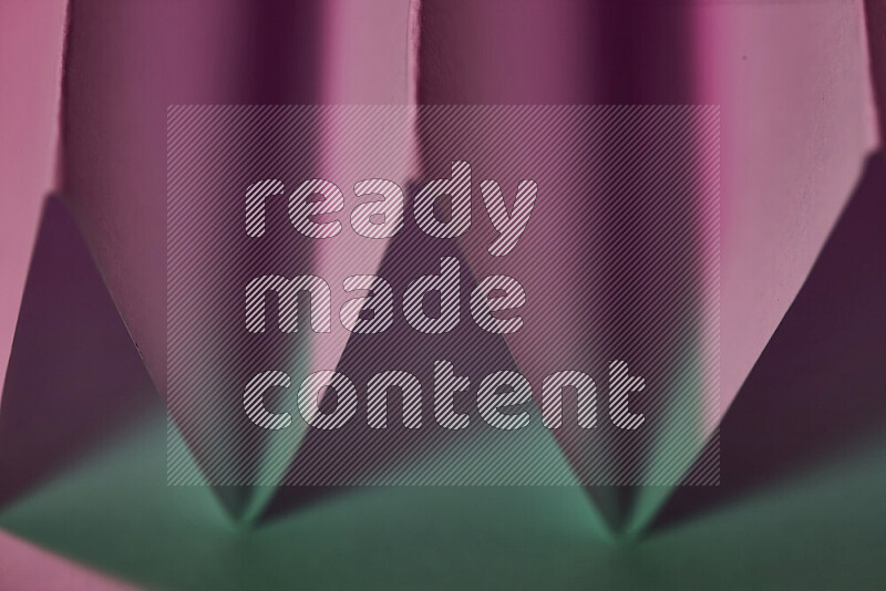 A close-up abstract image showing sharp geometric paper folds in green and pink gradients