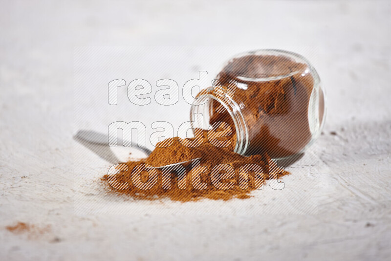 A glass jar full of ground paprika powder flipped with some spilling powder on white background