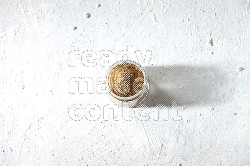 A glass jar full of cumin powder on textured white flooring