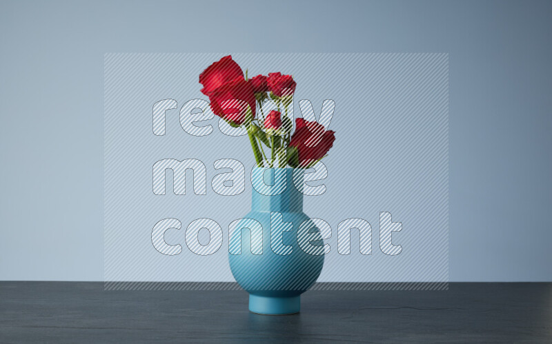 An arrangement of vivid red roses in a blue vase on black marble background