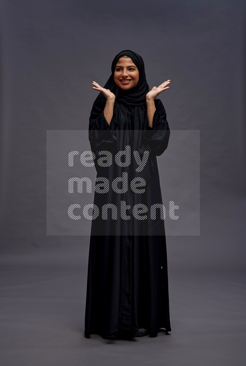 Saudi woman wearing Abaya standing hands behind head on gray background