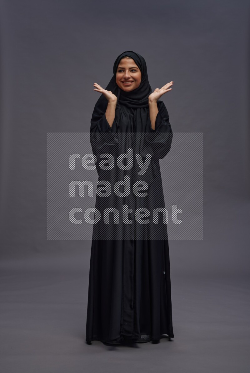 Saudi woman wearing Abaya standing hands behind head on gray background