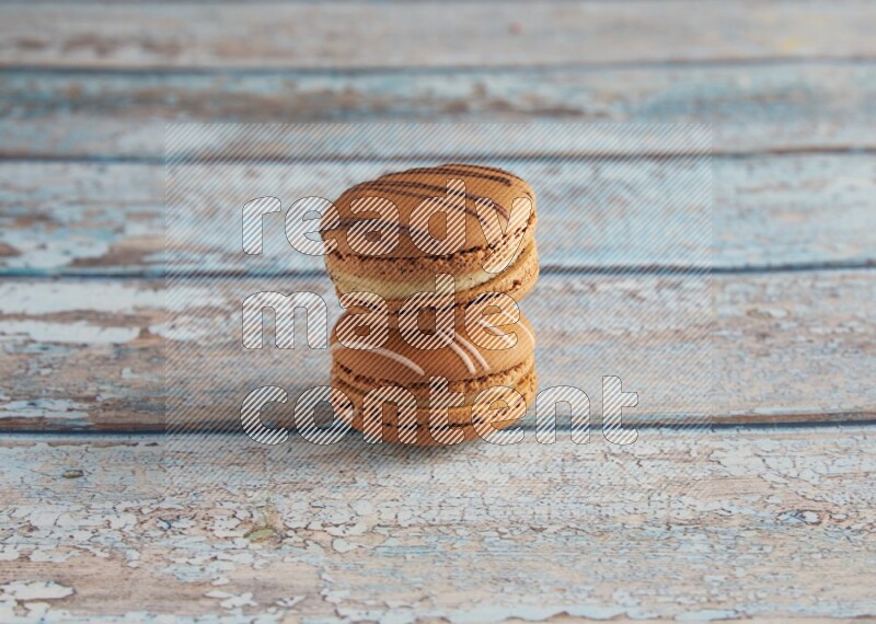 45º Shot of of two assorted Brown Irish Cream, and light brown Almond Cream macarons next to each other on light blue background