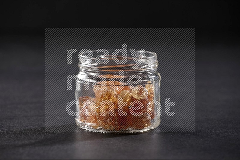 A glass jar filled with gum arabic on black flooring in different angles