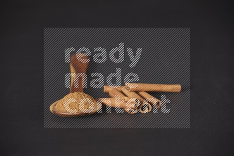 Cinnamon powder in a wooden ladle spoon beside it cinnamon sticks on the flooring on black background in different angles