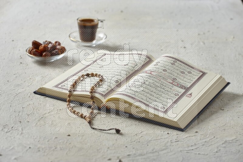 Quran with dates, prayer beads and different drinks all placed on textured white background