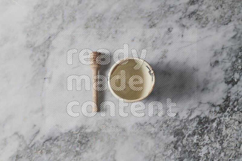 Decorative pottery bowl with wooden honey dipper on the side on grey marble background