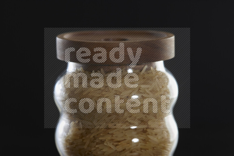 Basmati golden rice in a glass jar on black background