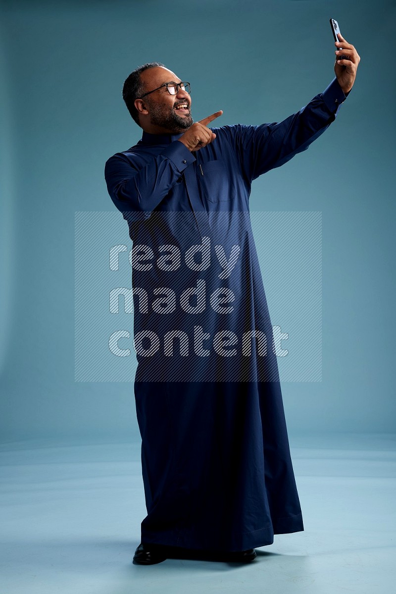Saudi Man without shimag Standing taking selfie on blue background