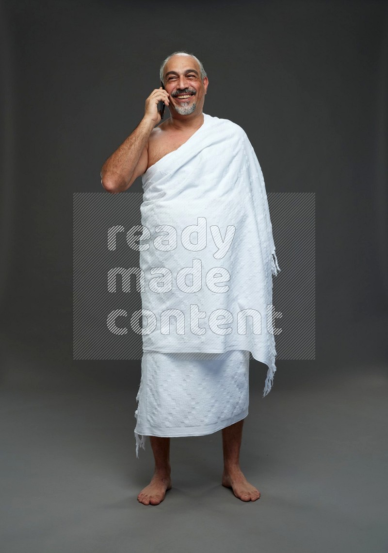 A man wearing Ehram Standing talking on phone on gray background