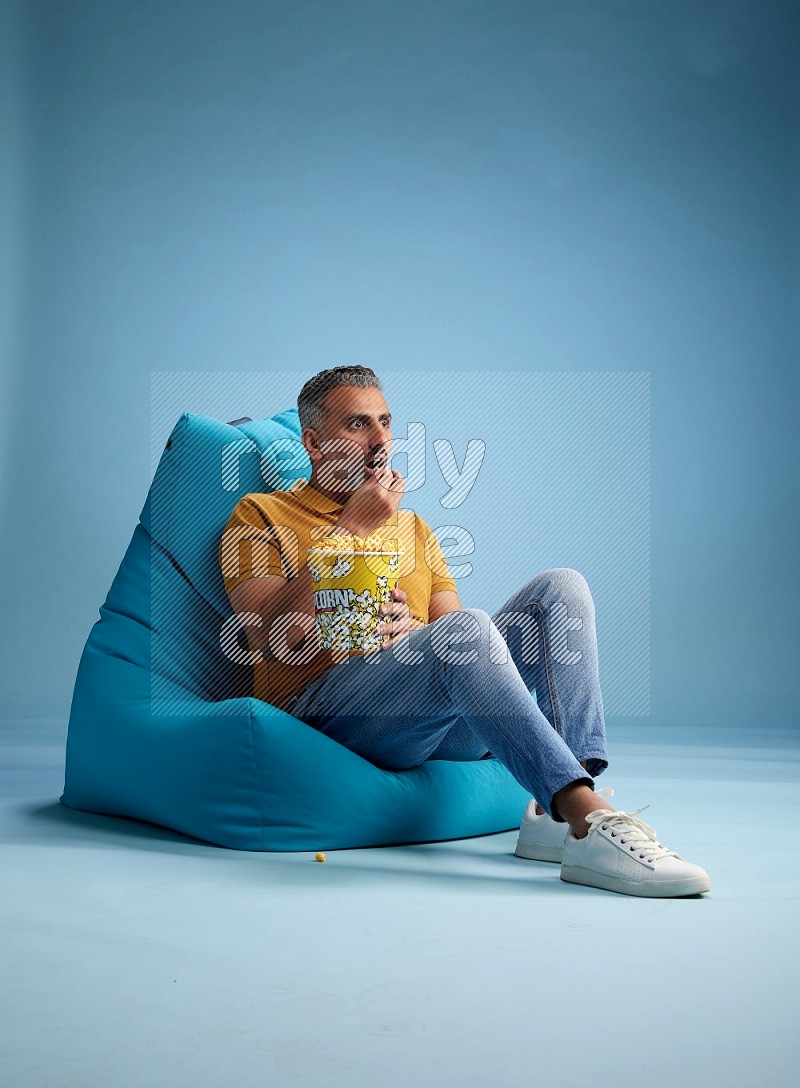 A man sitting on a blue beanbag and eating popcorn